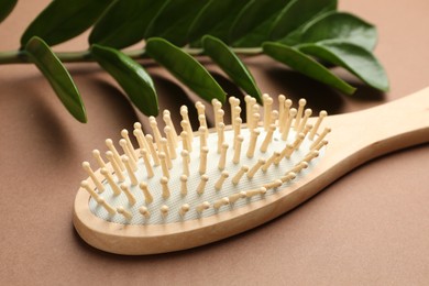 Photo of Wooden hair brush and green branch on dark beige background, closeup