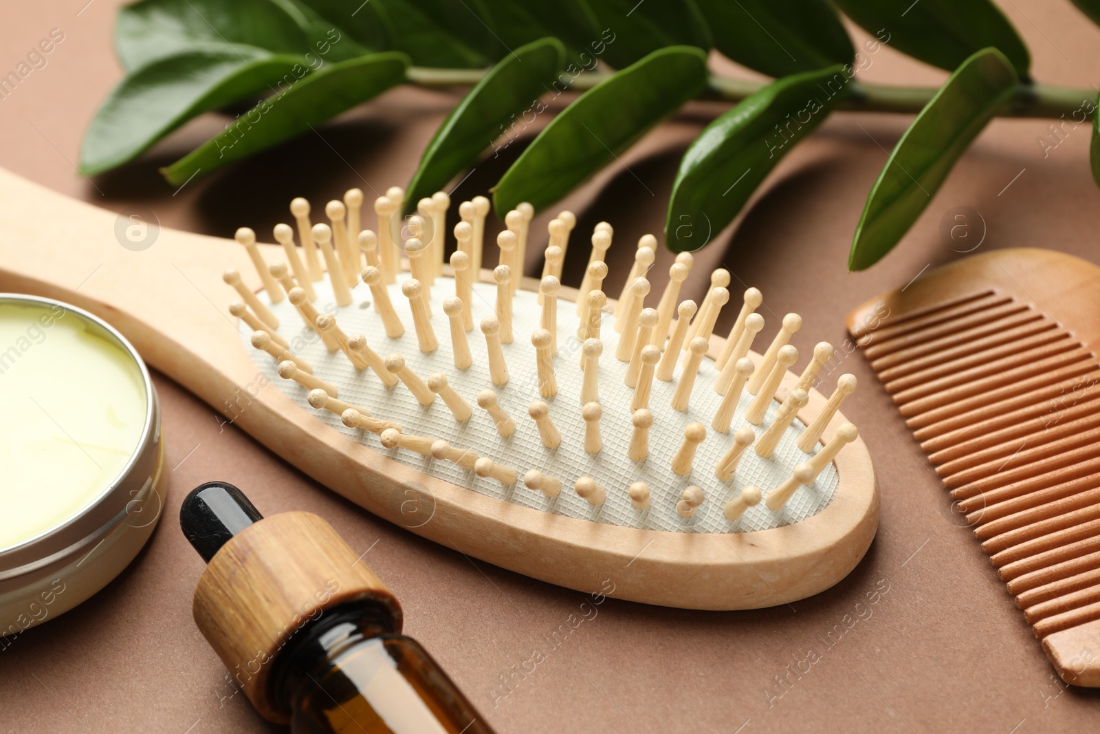 Photo of Wooden hair brush, comb, cosmetic products and green branch on dark beige background, closeup