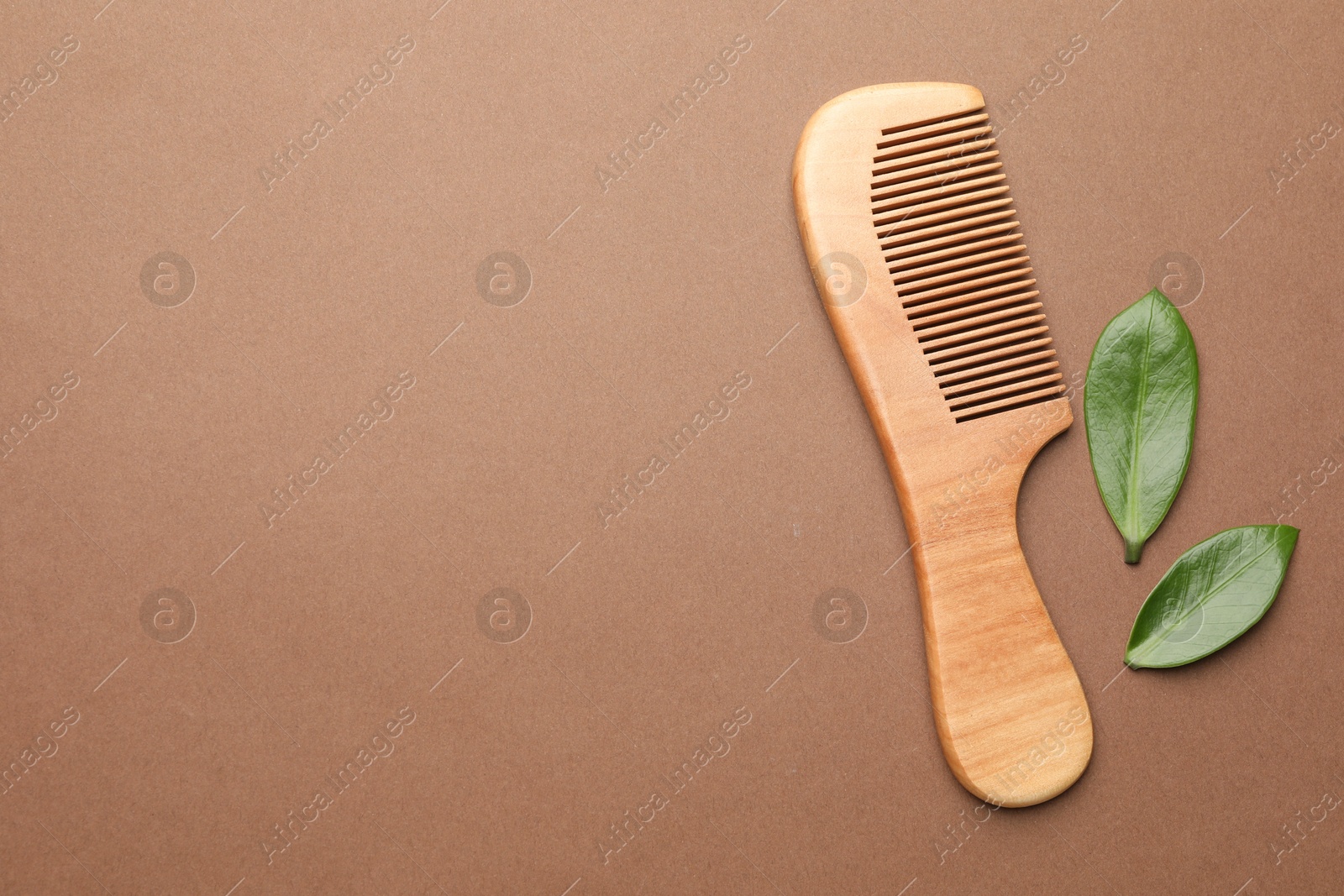 Photo of Wooden hair comb and green leaves on dark beige background, flat lay. Space for text