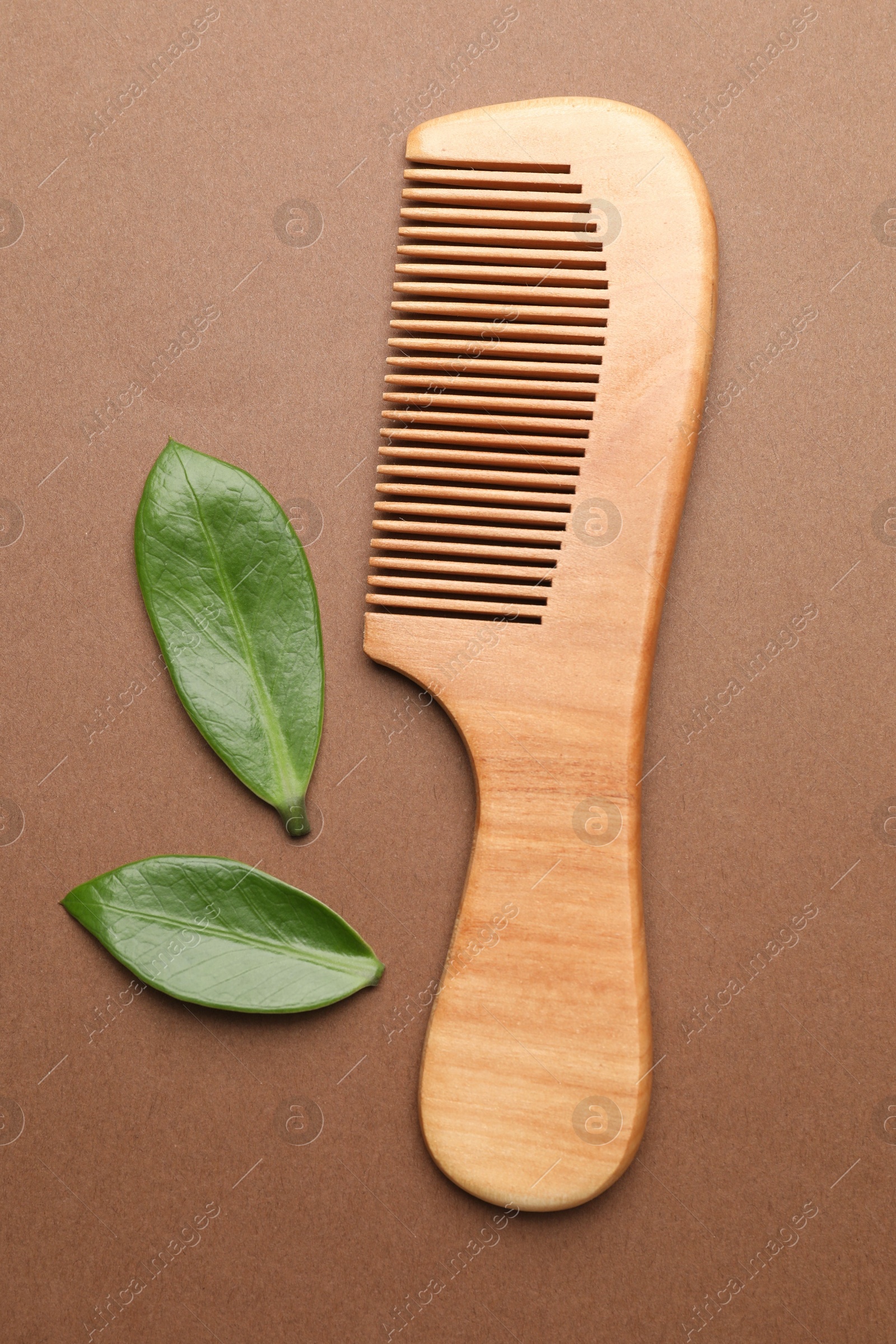 Photo of Wooden hair comb and green leaves on dark beige background, flat lay