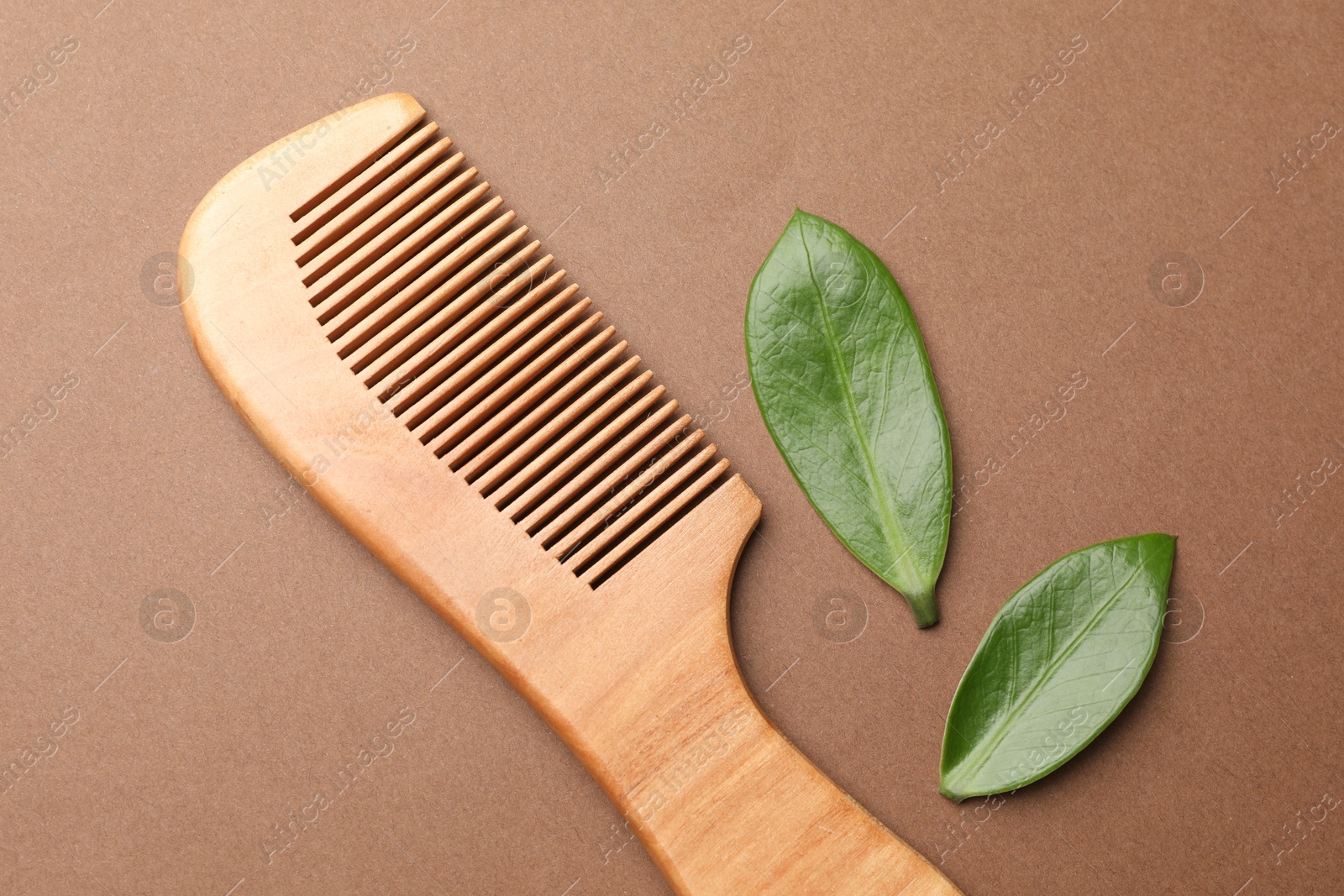 Photo of Wooden hair comb and green leaves on dark beige background, flat lay