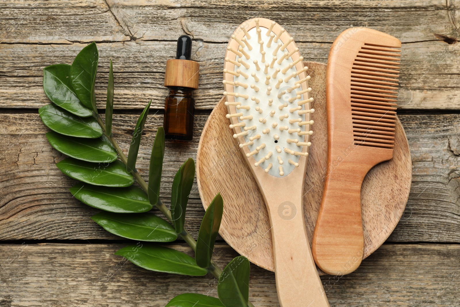 Photo of Hair brush, comb, cosmetic product and green branch on wooden table, flat lay