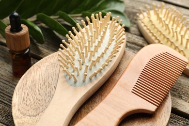 Photo of Hair brushes, comb, cosmetic product and green branch on wooden table, closeup