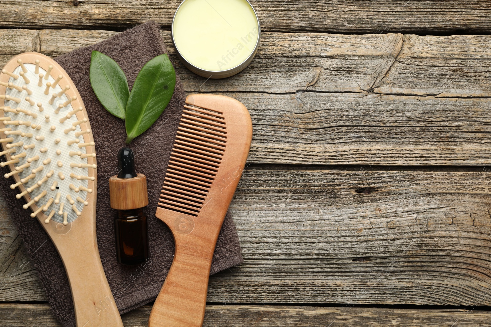 Photo of Hair brush, comb, cosmetic products, towel and green leaves on wooden table, flat lay. Space for text