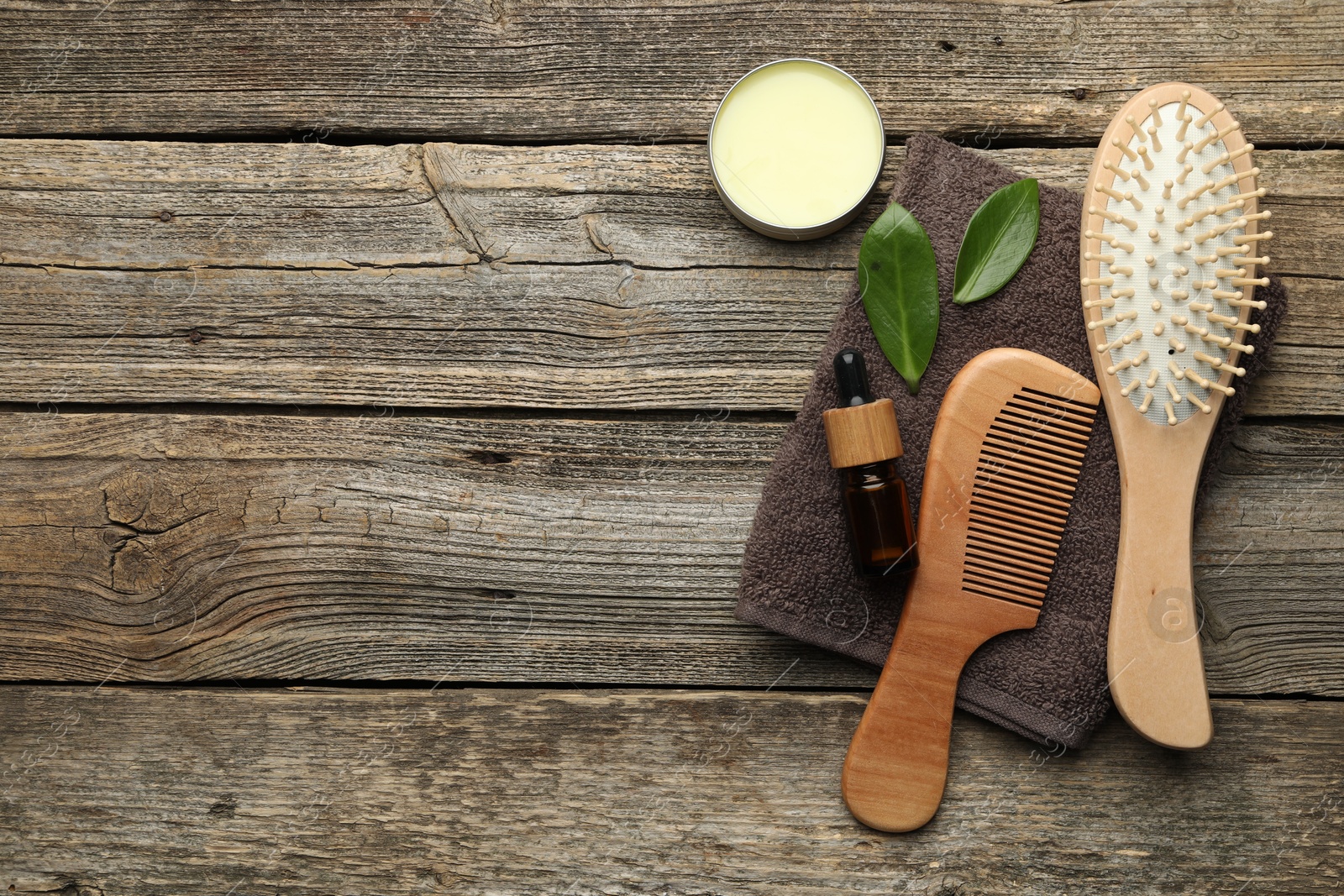 Photo of Hair brush, comb, cosmetic products, towel and green leaves on wooden table, flat lay. Space for text