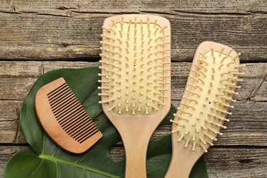 Photo of Hair brushes, comb and monstera leaf on wooden table, flat lay