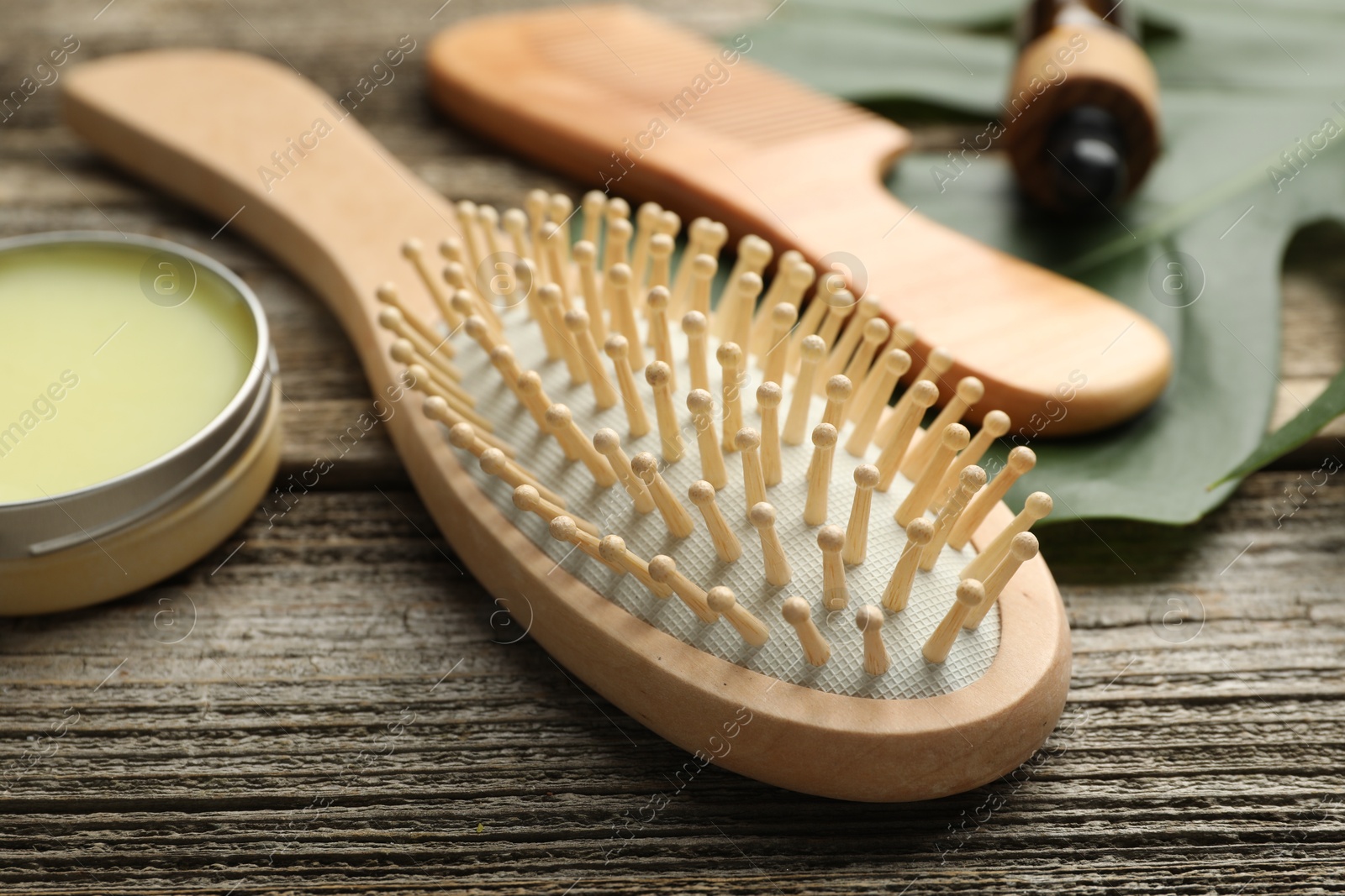 Photo of Hair brush, comb, wax and monstera leaf on wooden table, closeup