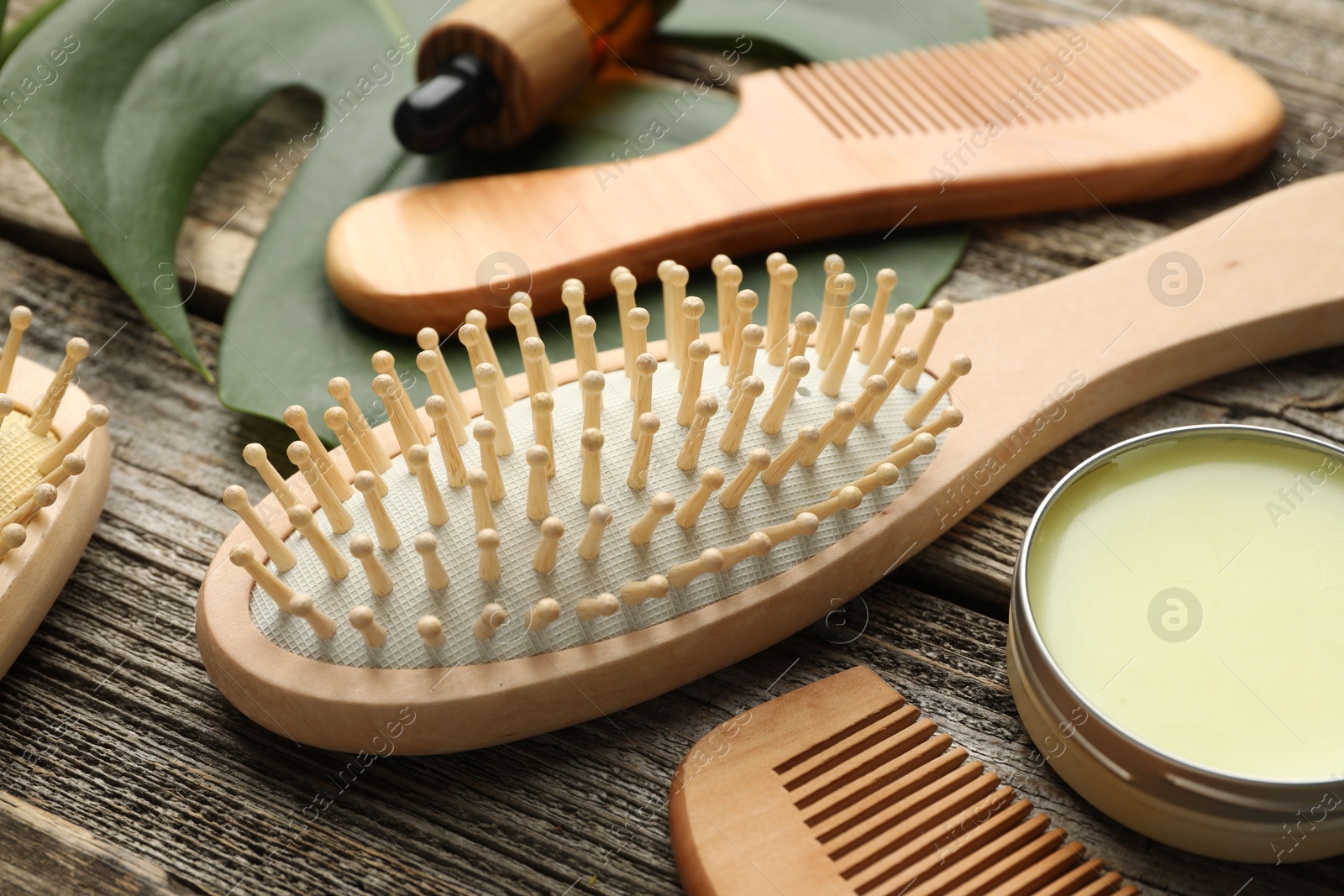 Photo of Hair brush, combs, wax and monstera leaf on wooden table, closeup