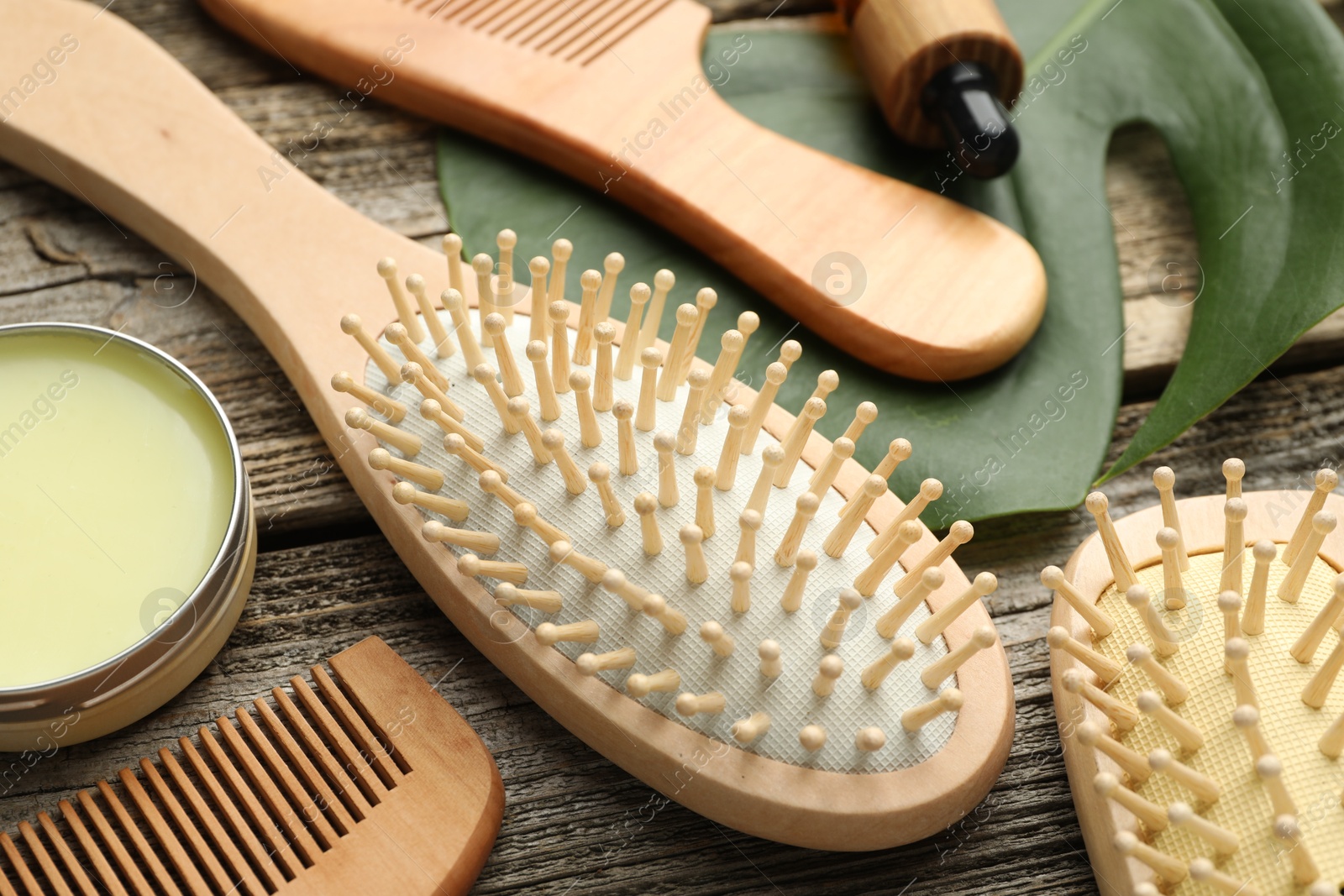 Photo of Hair brushes, combs, wax and monstera leaf on wooden table, closeup