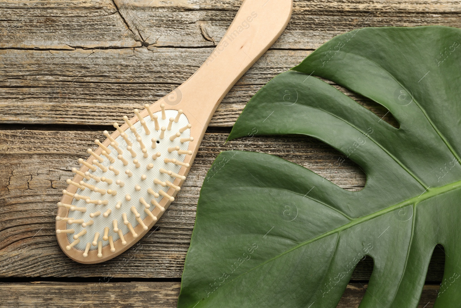 Photo of Hair brush and monstera leaf on wooden table, top view