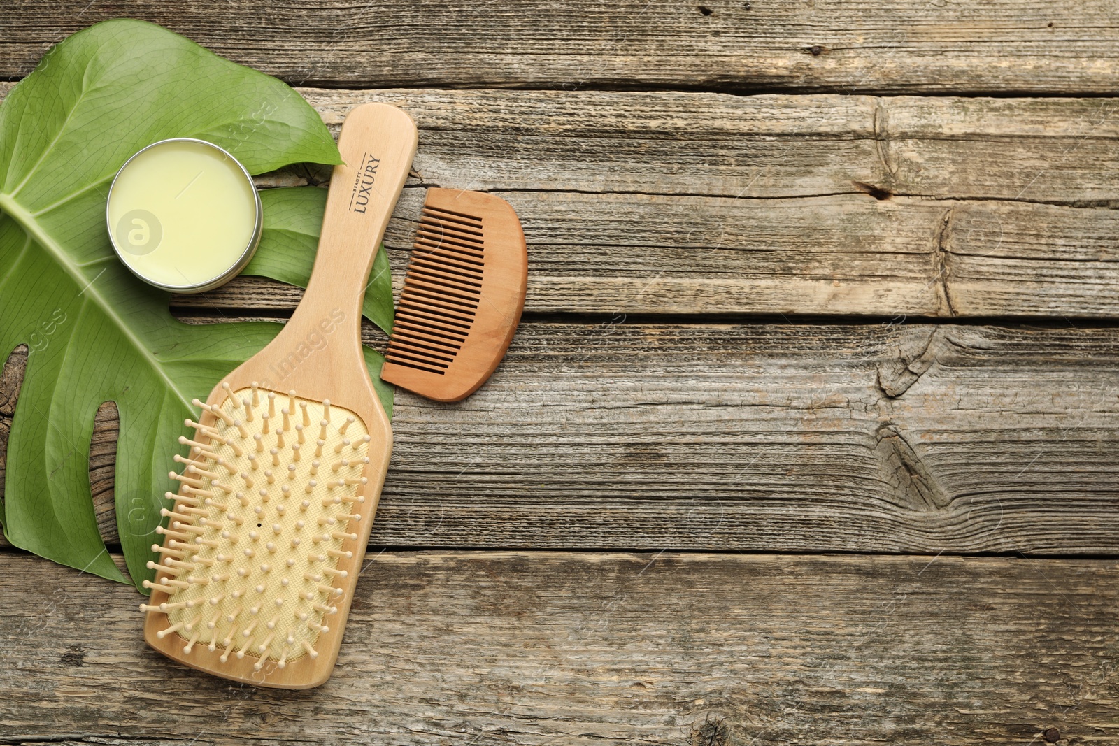 Photo of Hair brush, comb, wax and monstera leaf on wooden table, flat lay. Space for text