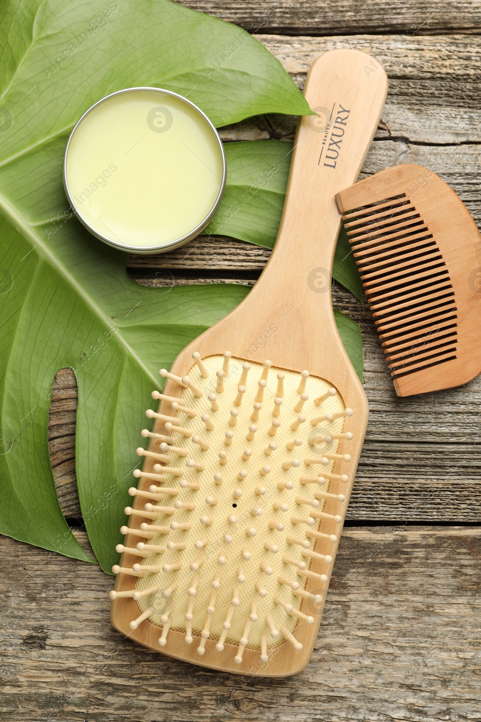 Photo of Hair brush, comb, wax and monstera leaf on wooden table, flat lay