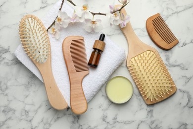 Photo of Wooden hair brushes, combs, cosmetic products, towel and orchid branch on white marble table, flat lay