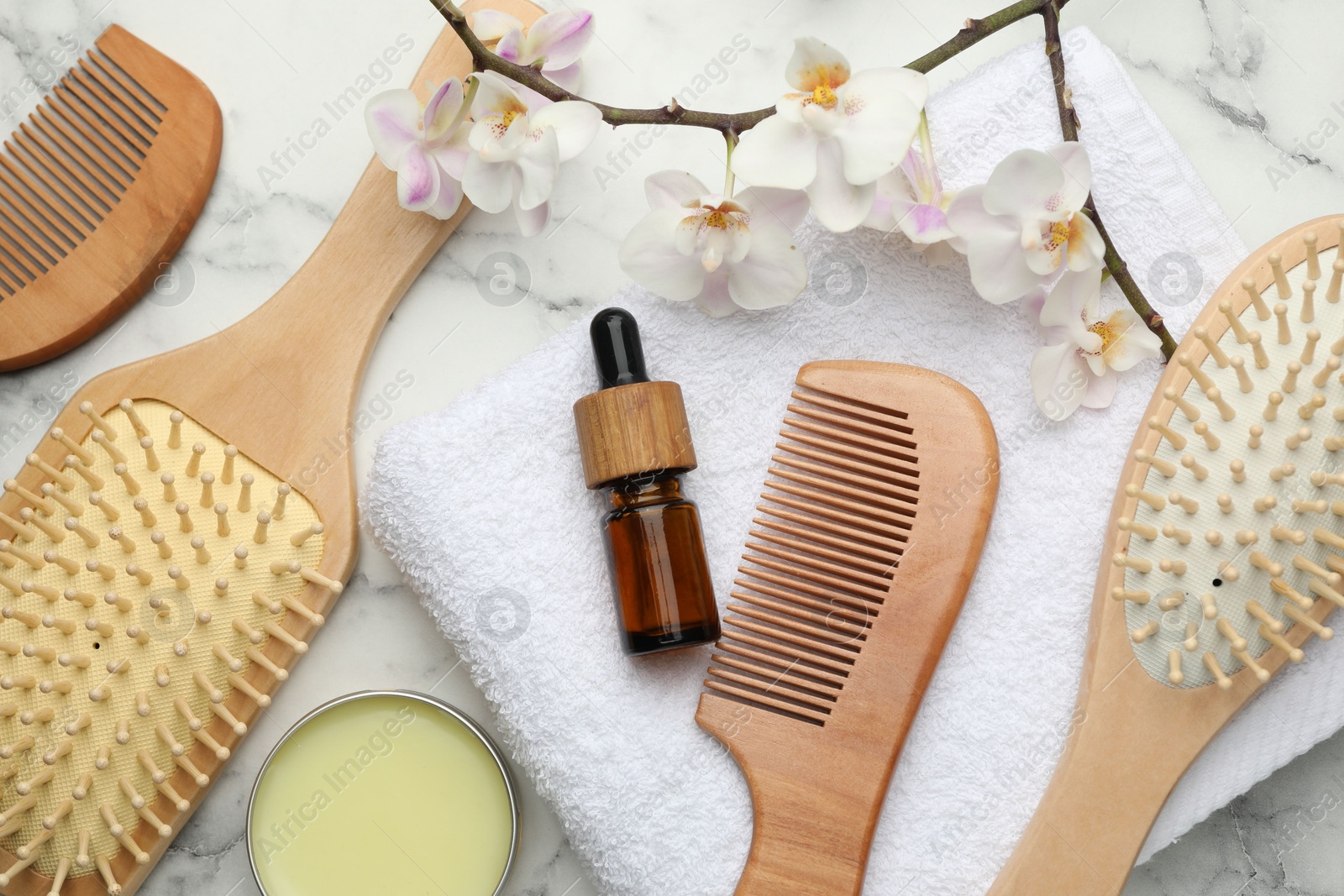 Photo of Wooden hair brushes, combs, cosmetic products, towel and orchid branch on white marble table, flat lay