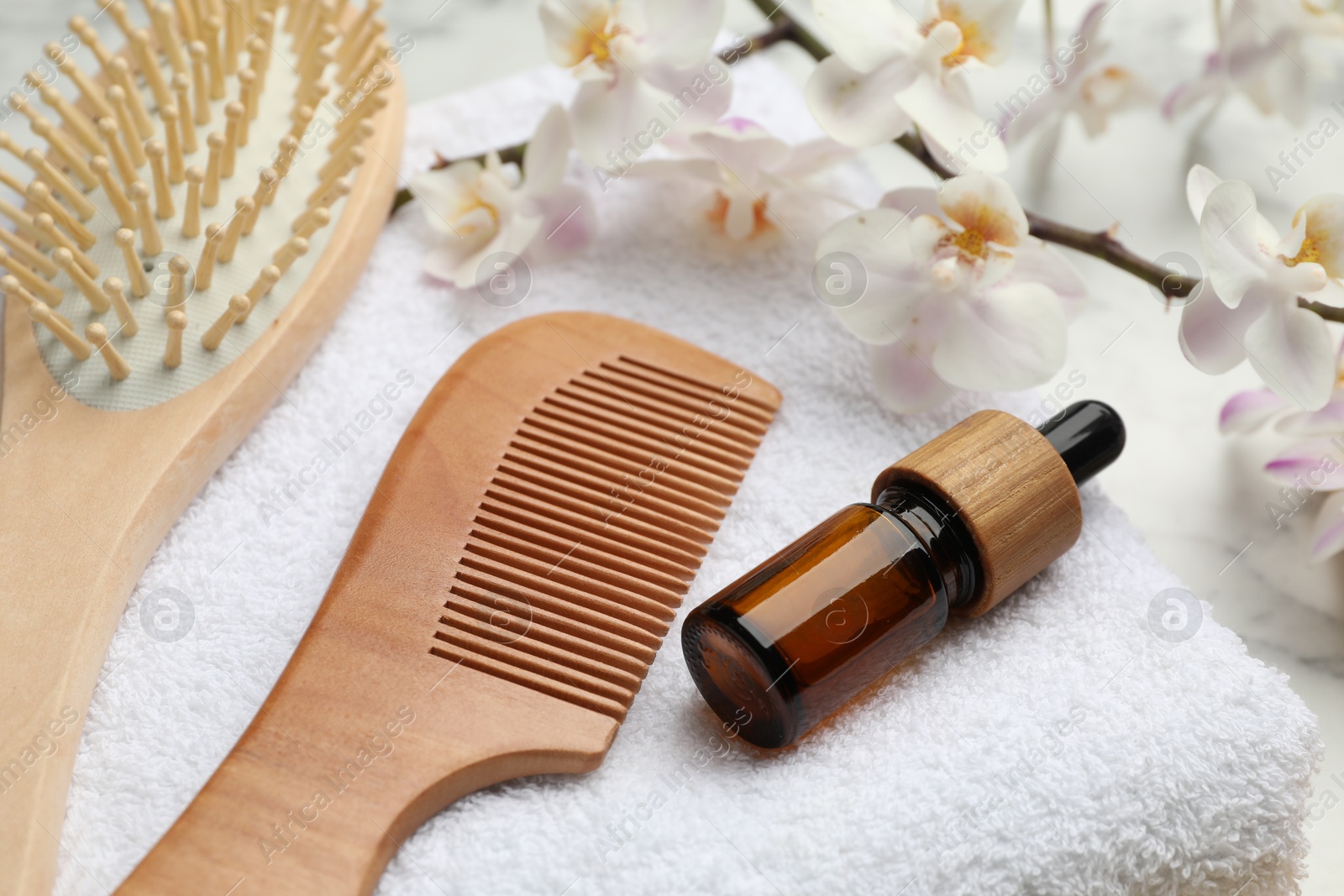 Photo of Wooden hair brush, comb, cosmetic products, towel and orchid branch on white marble table, closeup