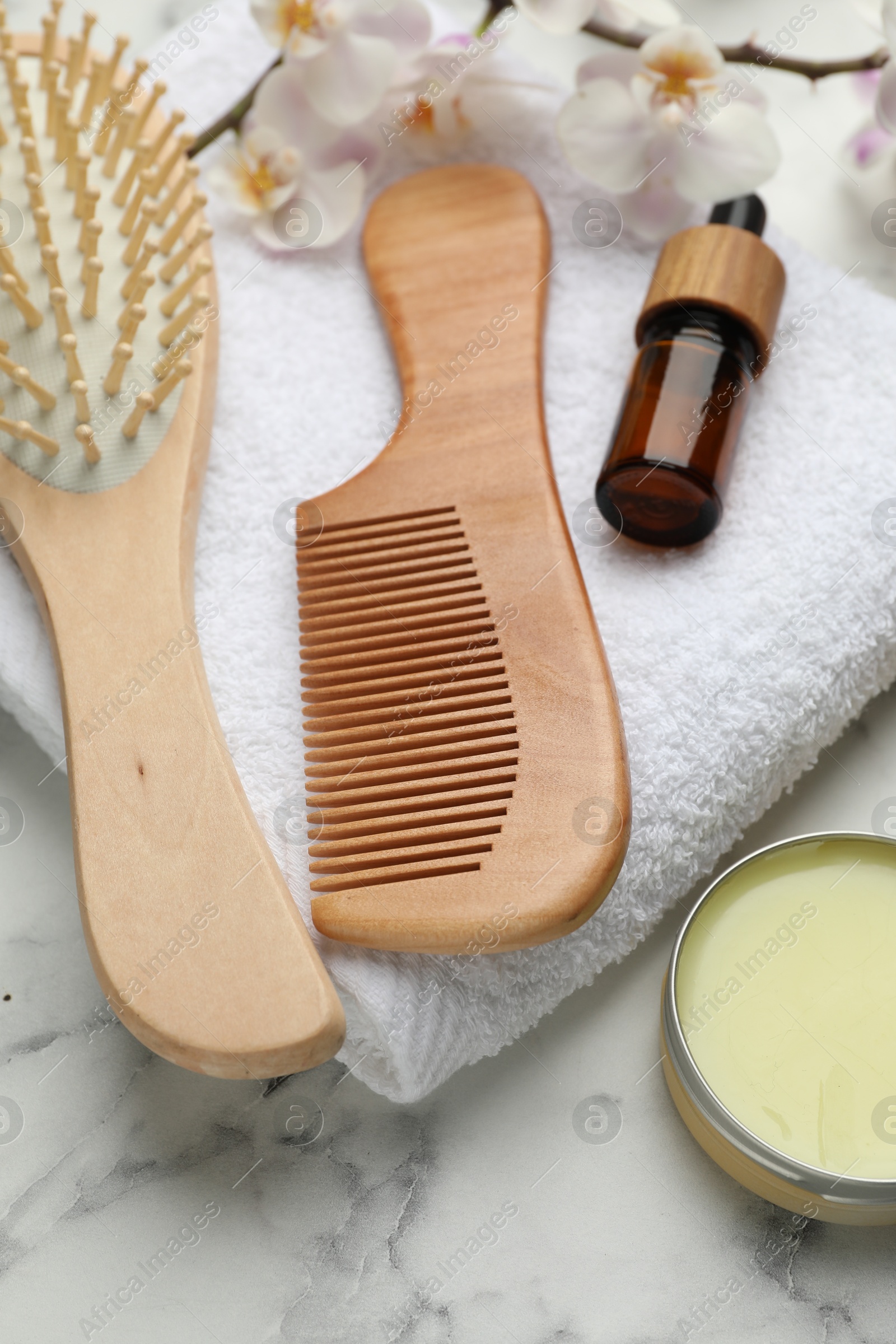 Photo of Wooden hair brush, comb, cosmetic products, towel and orchid branch on white marble table, closeup