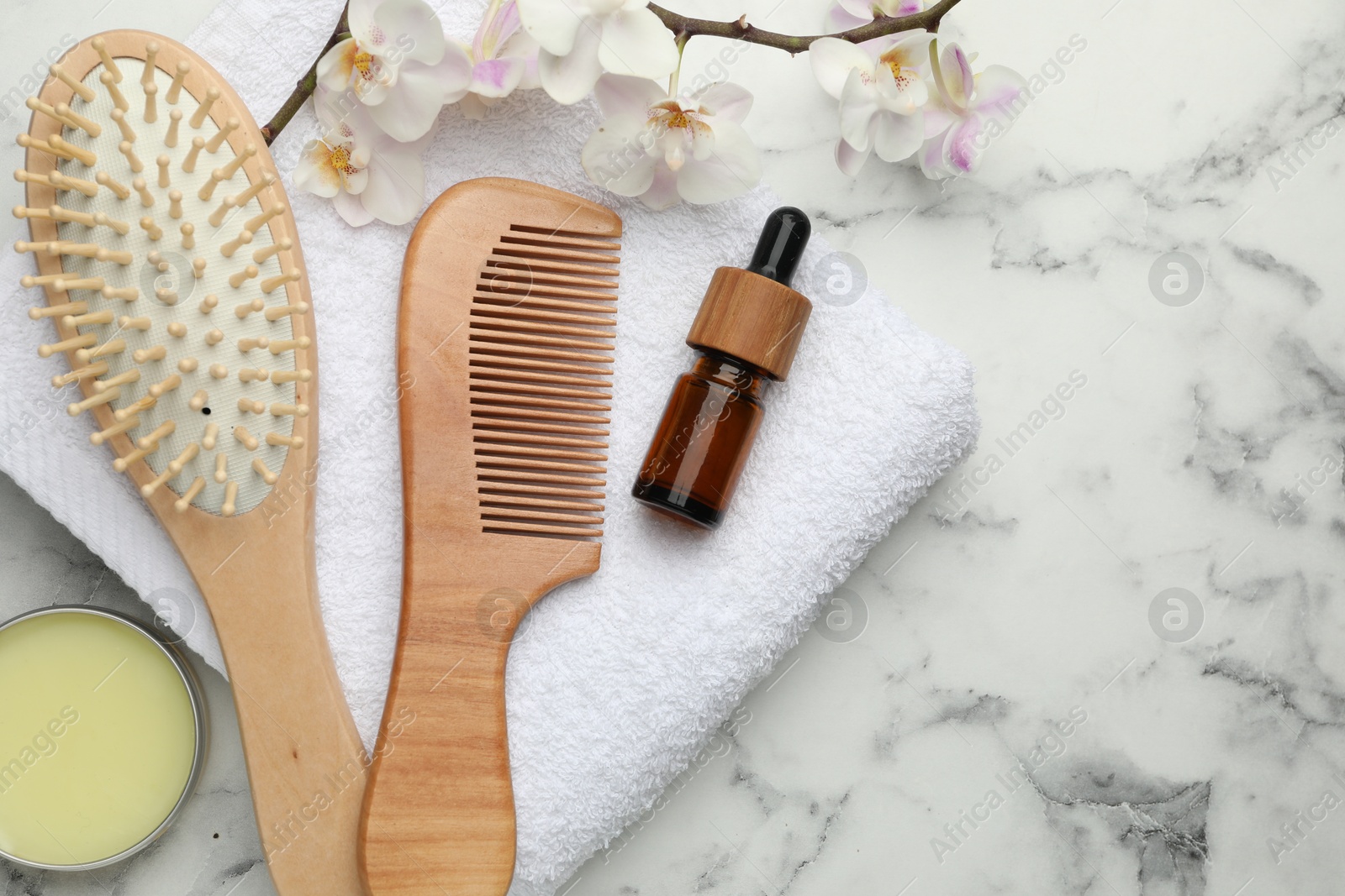 Photo of Wooden hair brush, comb, cosmetic products, towel and orchid branch on white marble table, flat lay. Space for text