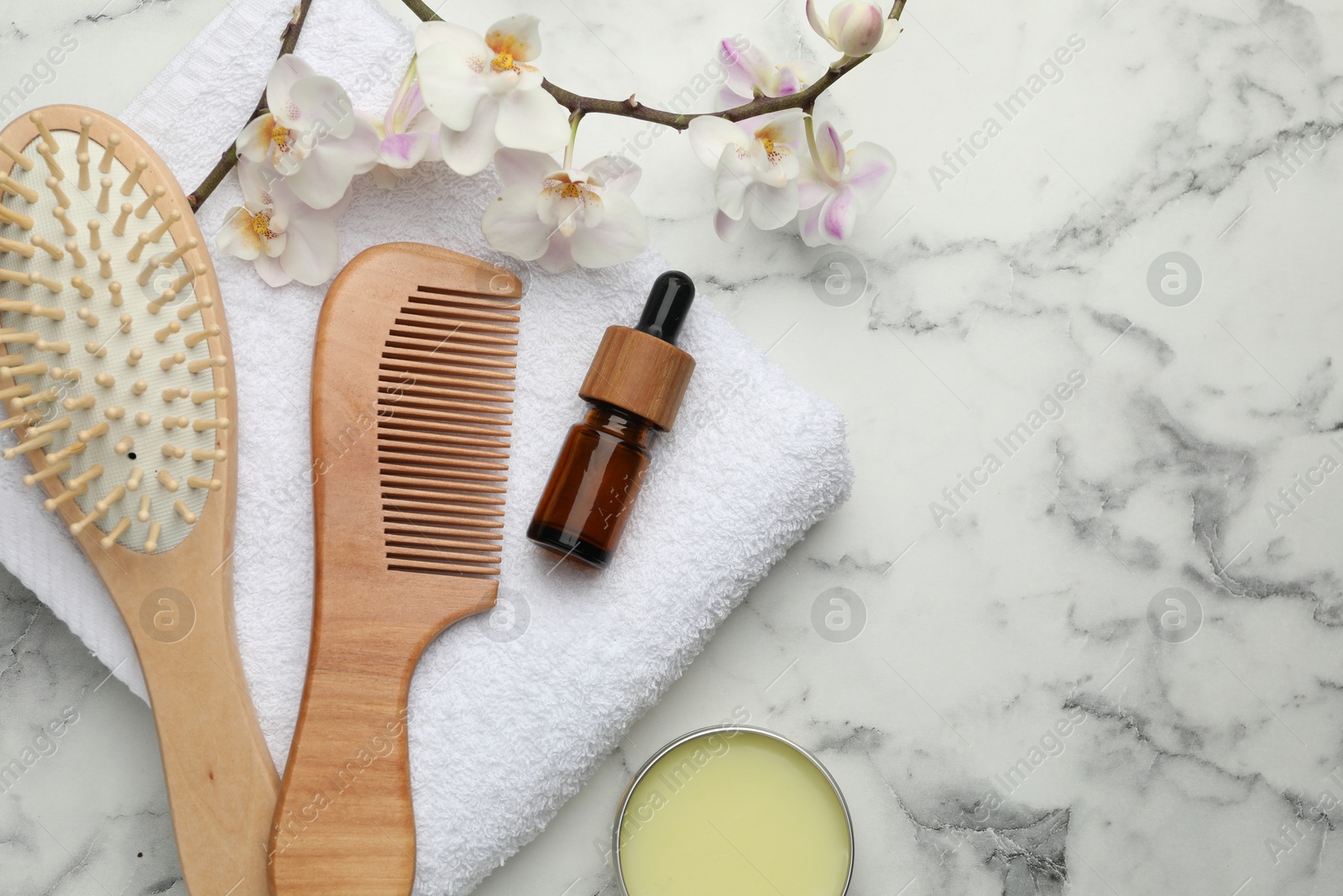 Photo of Wooden hair brush, comb, cosmetic products, towel and orchid branch on white marble table, flat lay. Space for text