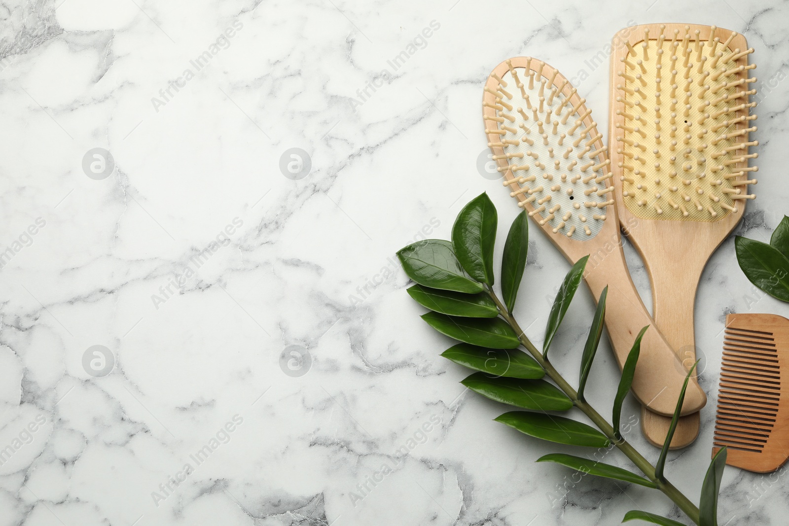 Photo of Wooden hair brushes, comb and green leaves on white marble table, flat lay. Space for text