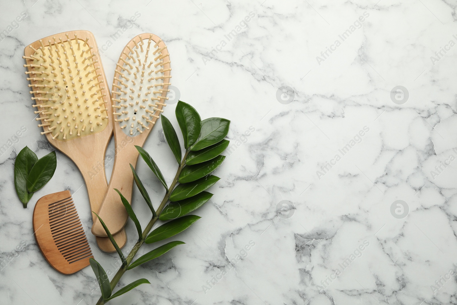 Photo of Wooden hair brushes, comb and green leaves on white marble table, flat lay. Space for text