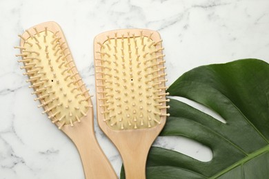 Photo of Wooden hair brushes and monstera leaf on white marble table, flat lay