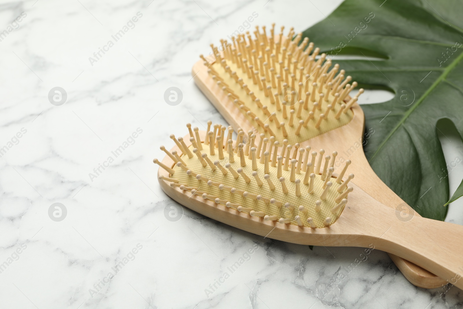 Photo of Wooden hair brushes and monstera leaf on white marble table, closeup. Space for text