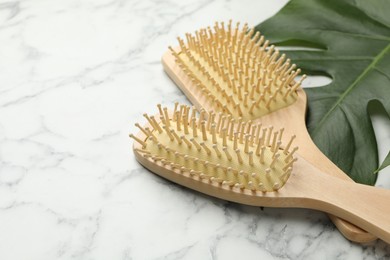 Photo of Wooden hair brushes and monstera leaf on white marble table, closeup. Space for text