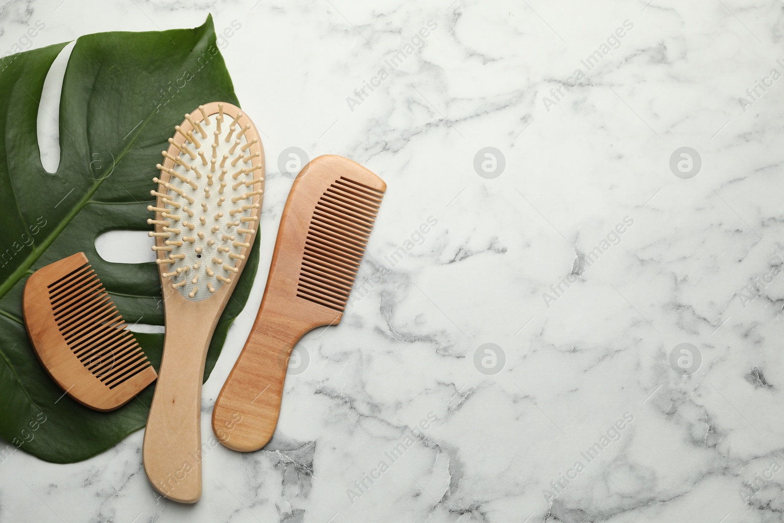 Photo of Wooden hair brush, combs and monstera leaf on white marble table, flat lay. Space for text