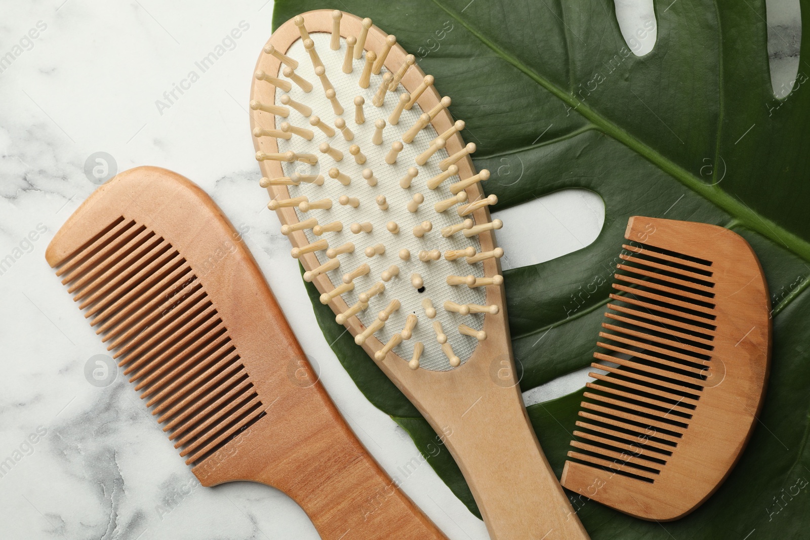 Photo of Wooden hair brush, combs and monstera leaf on white marble table, flat lay