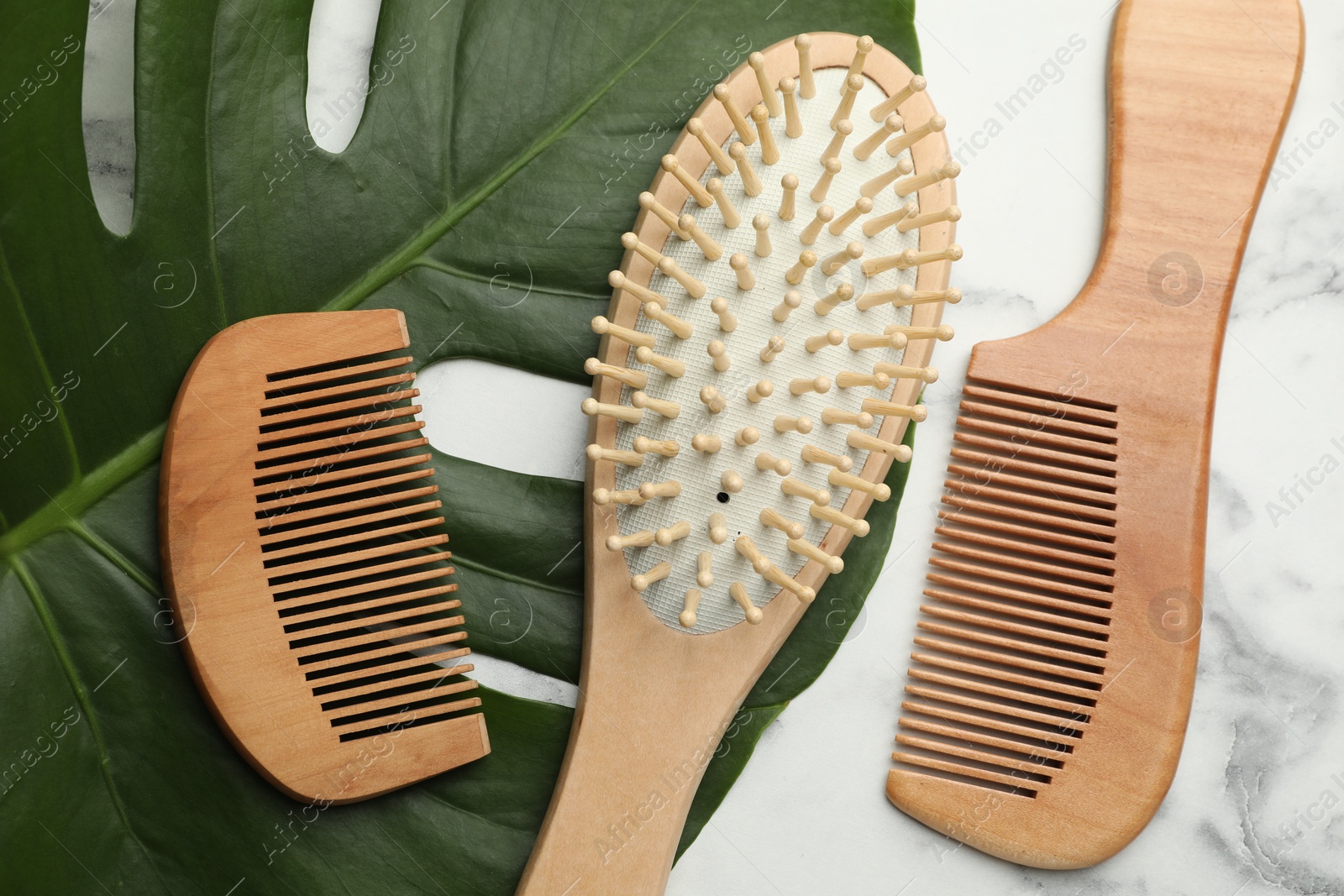 Photo of Wooden hair brush, combs and monstera leaf on white marble table, flat lay