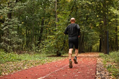 Photo of Athletic man running in park, back view. Space for text