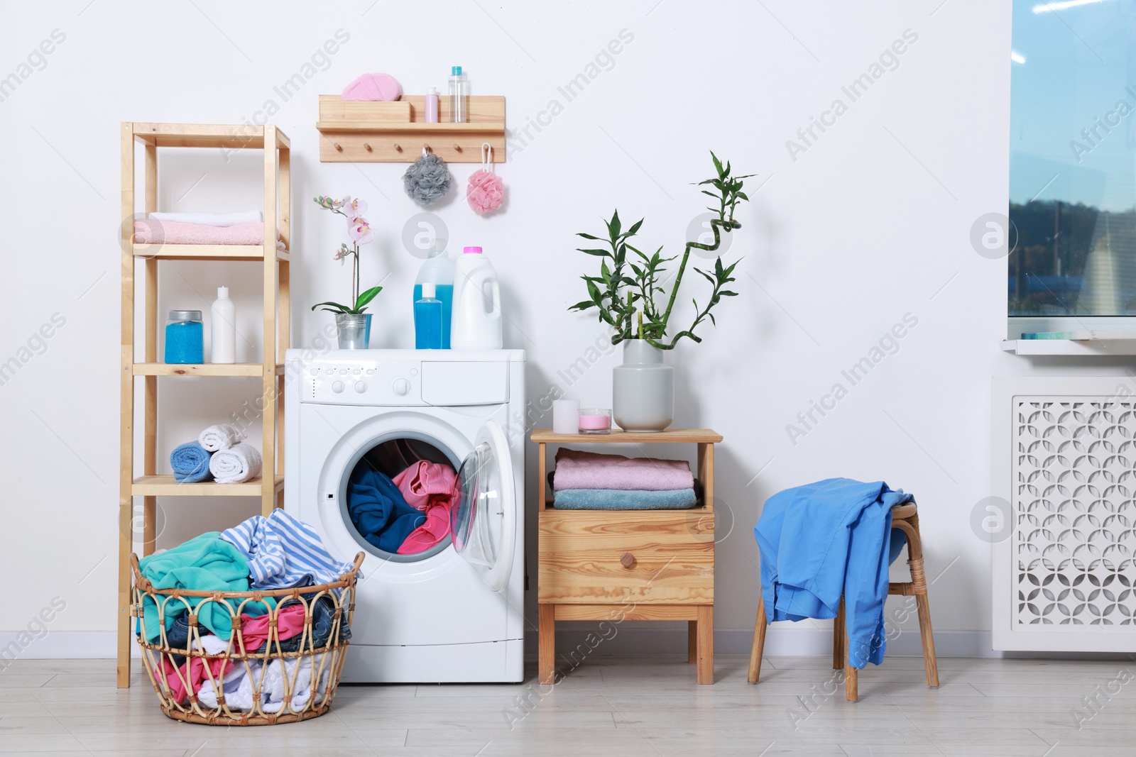 Photo of Washing machine, detergents, clean towels and basket with laundry in room