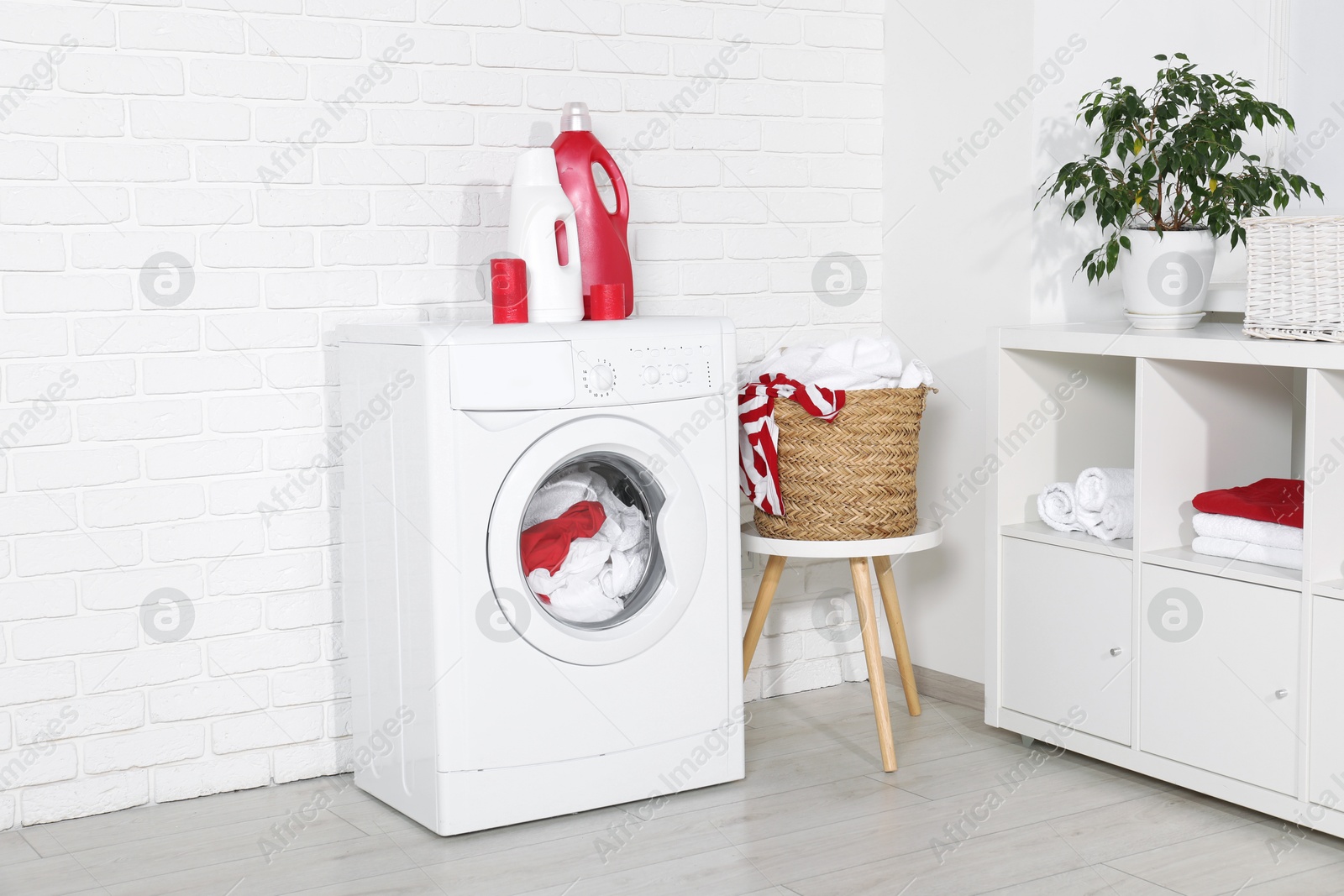 Photo of Washing machine, detergents and basket with laundry in room