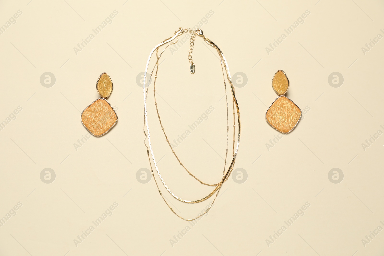 Photo of Stylish golden necklace and earrings on beige background, flat lay