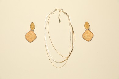 Photo of Stylish golden necklace and earrings on beige background, flat lay