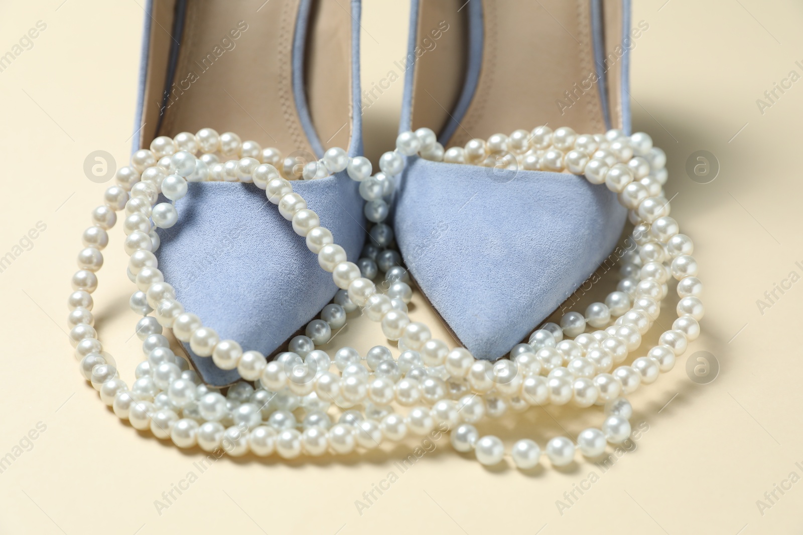 Photo of Stylish shoes and pearl necklace on beige background, closeup