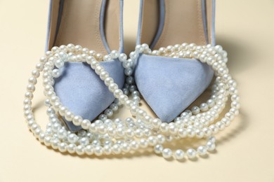 Photo of Stylish shoes and pearl necklace on beige background, closeup