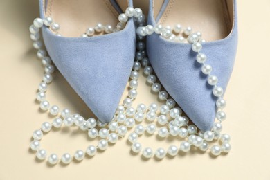 Photo of Stylish shoes and pearl necklace on beige background, closeup