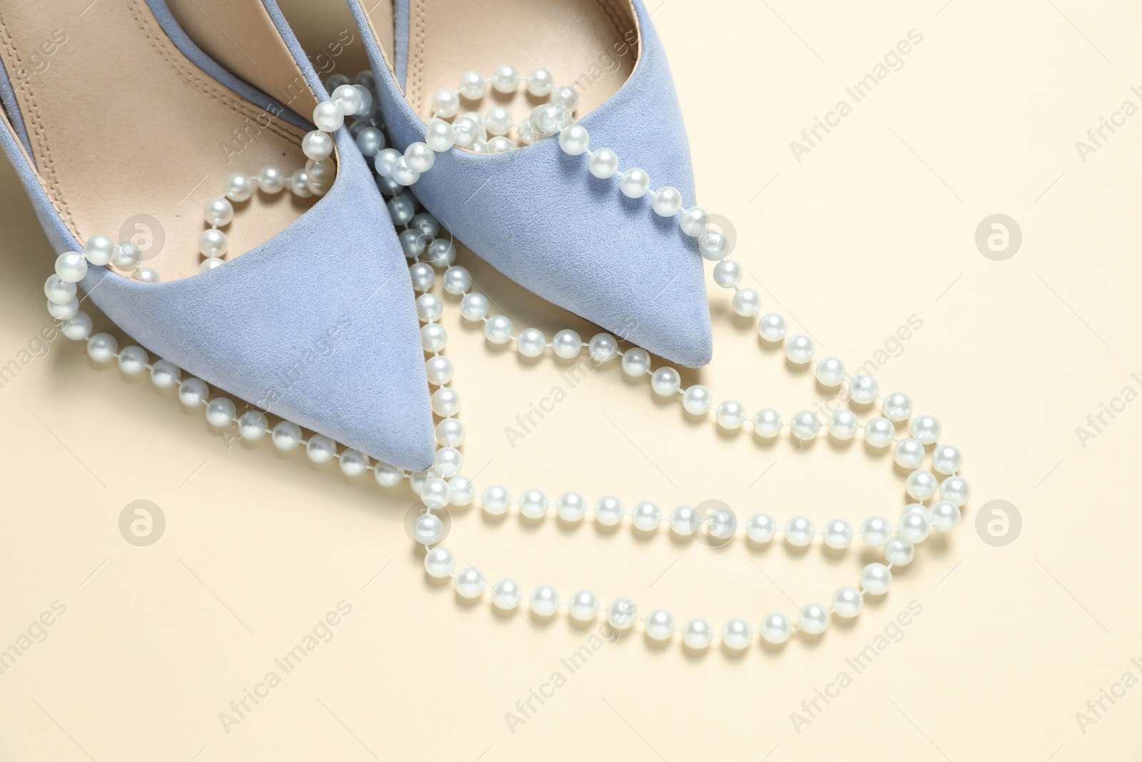 Photo of Stylish shoes and pearl necklace on beige background, closeup