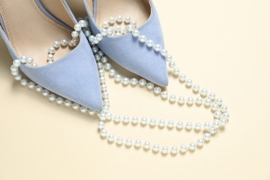 Photo of Stylish shoes and pearl necklace on beige background, closeup