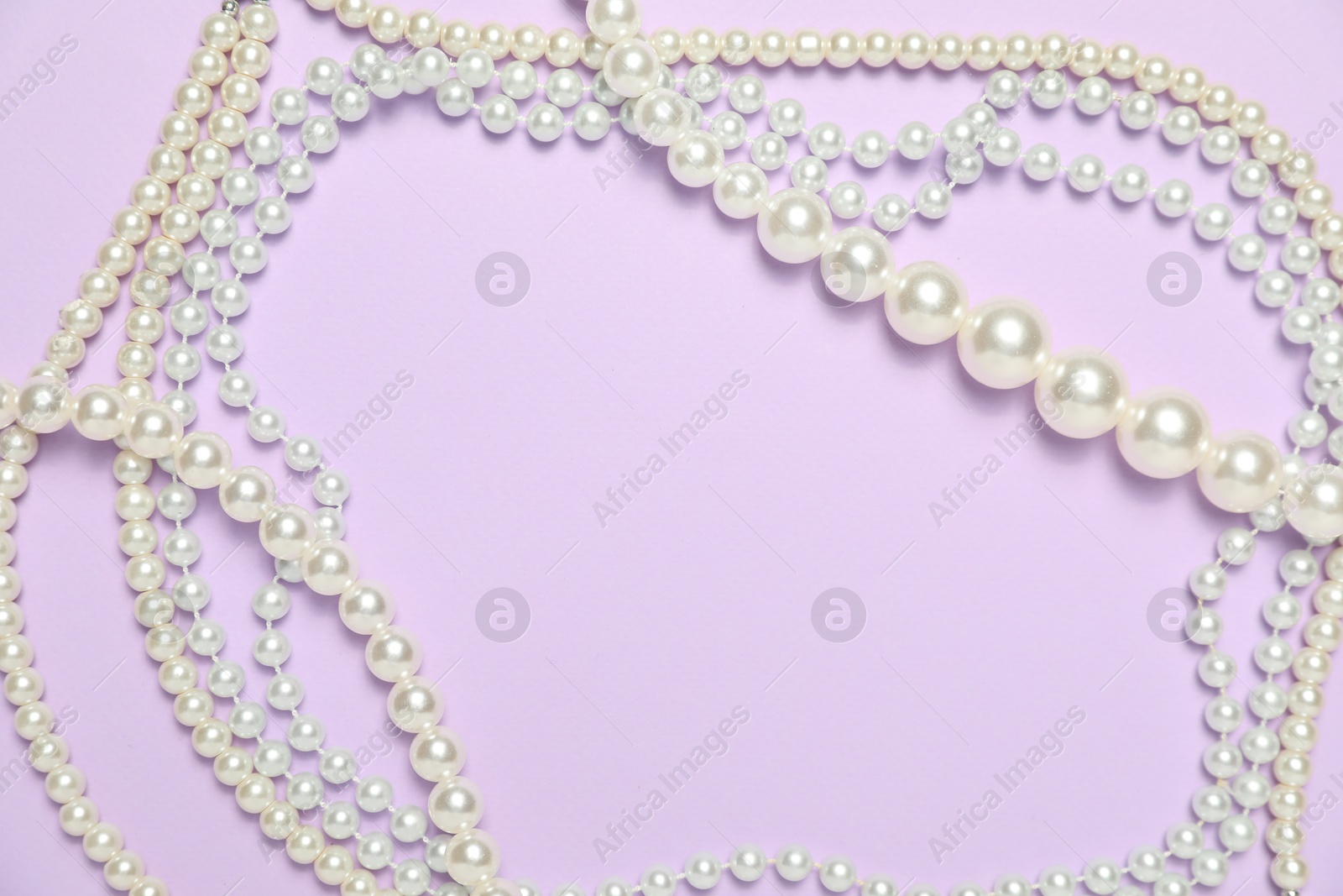 Photo of Beautiful pearl necklaces on violet background, flat lay. Space for text