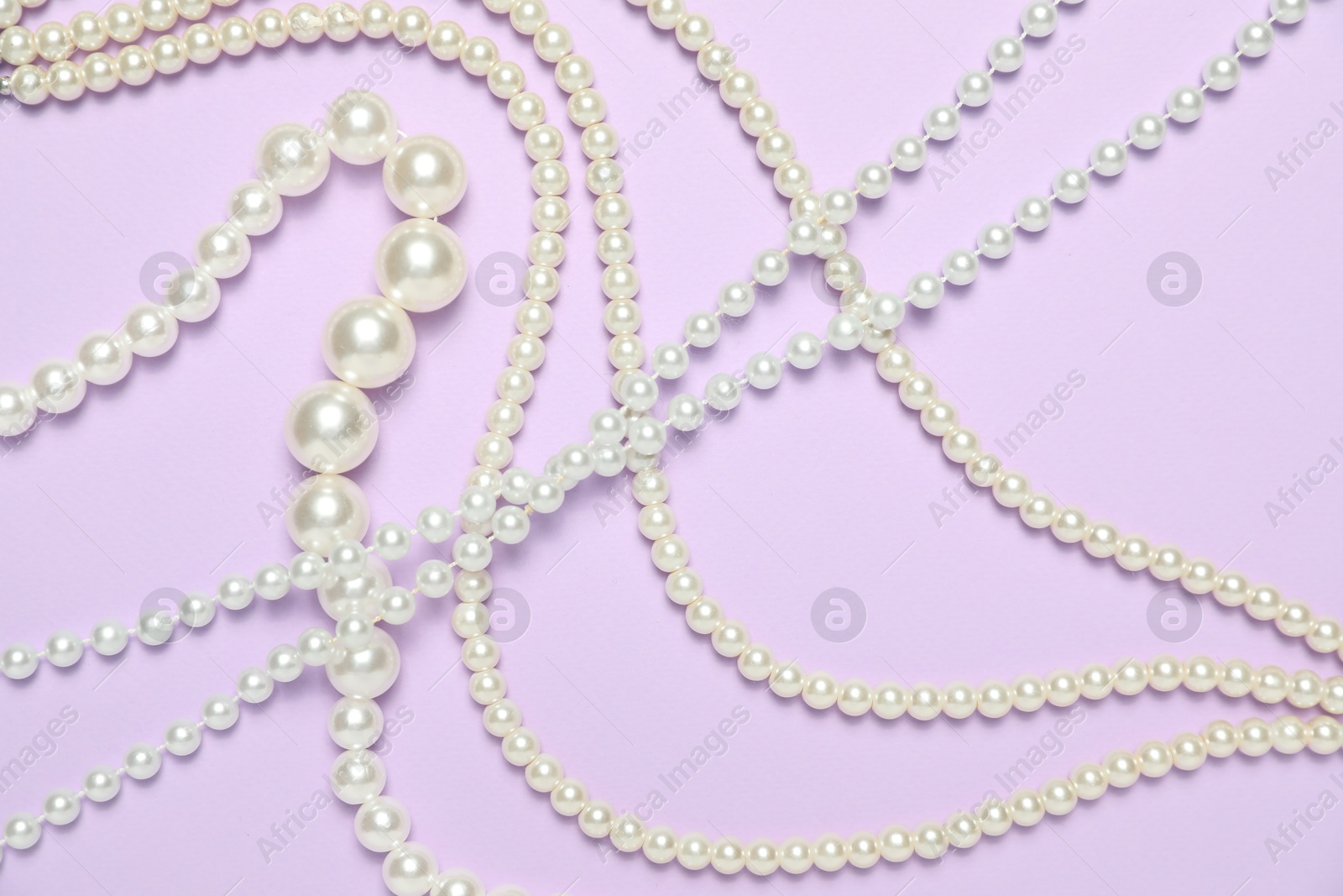 Photo of Beautiful pearl necklaces on violet background, flat lay