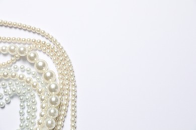 Photo of Beautiful pearl necklaces on white background, flat lay. Space for text