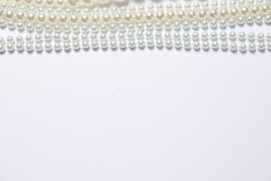 Photo of Beautiful pearl necklaces on white background, flat lay. Space for text