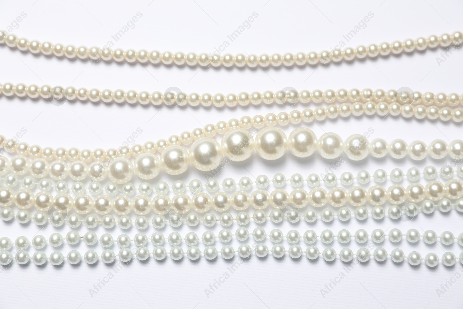 Photo of Beautiful pearl necklaces on white background, flat lay