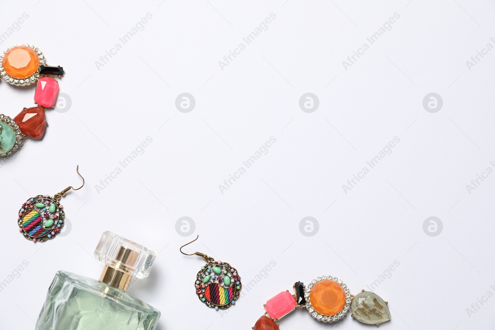 Photo of Bottle of perfume and stylish earrings on white background, flat lay. Space for text