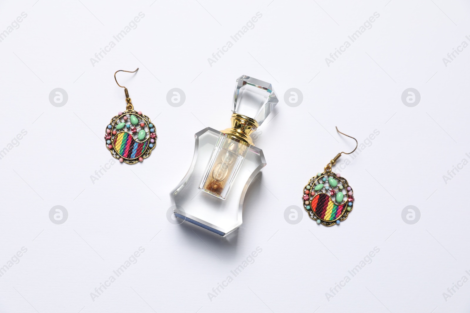 Photo of Bottle of perfume and stylish earrings on white background, flat lay