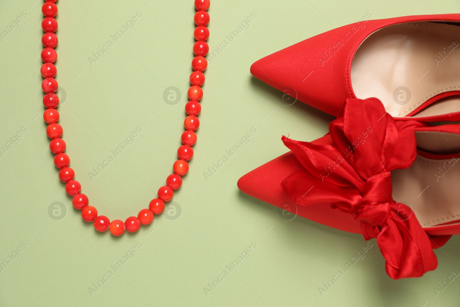 Photo of Stylish red women's shoes and necklace on light green background, flat lay