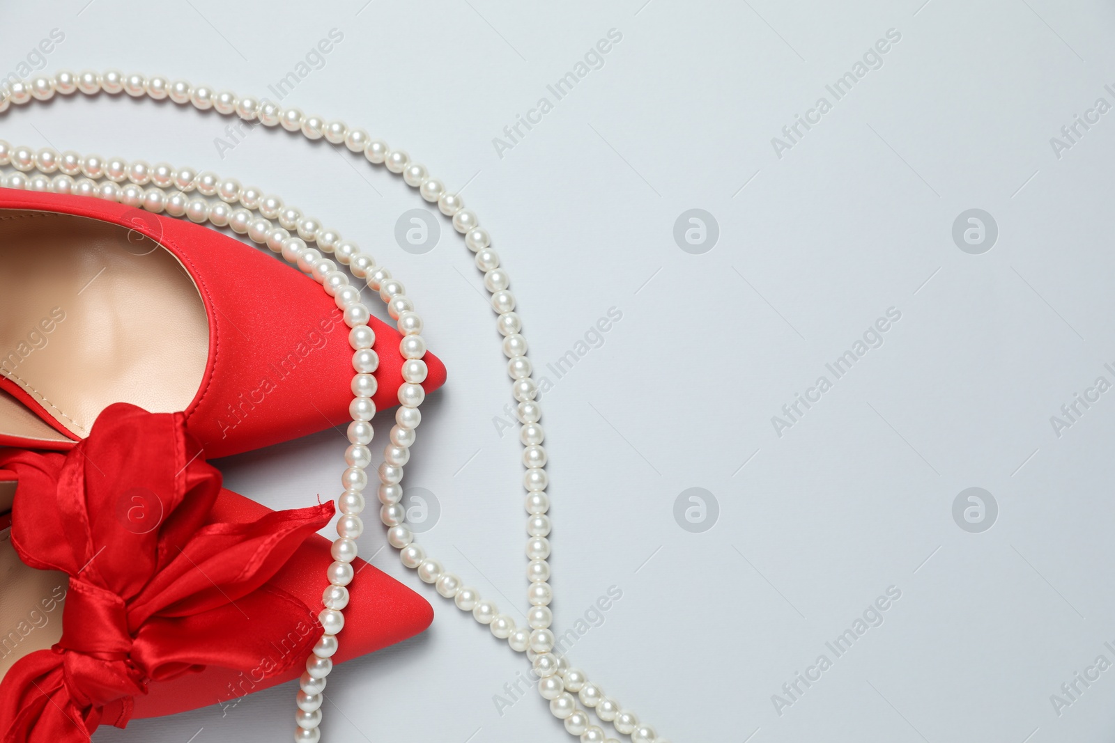 Photo of Stylish red women's shoes and pearl necklace on light grey background, flat lay. Space for text