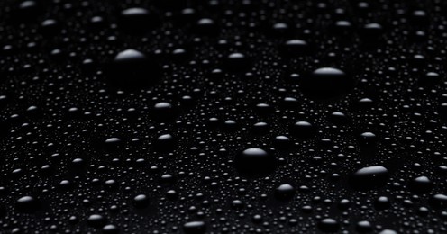 Photo of Water drops on black glass surface, closeup